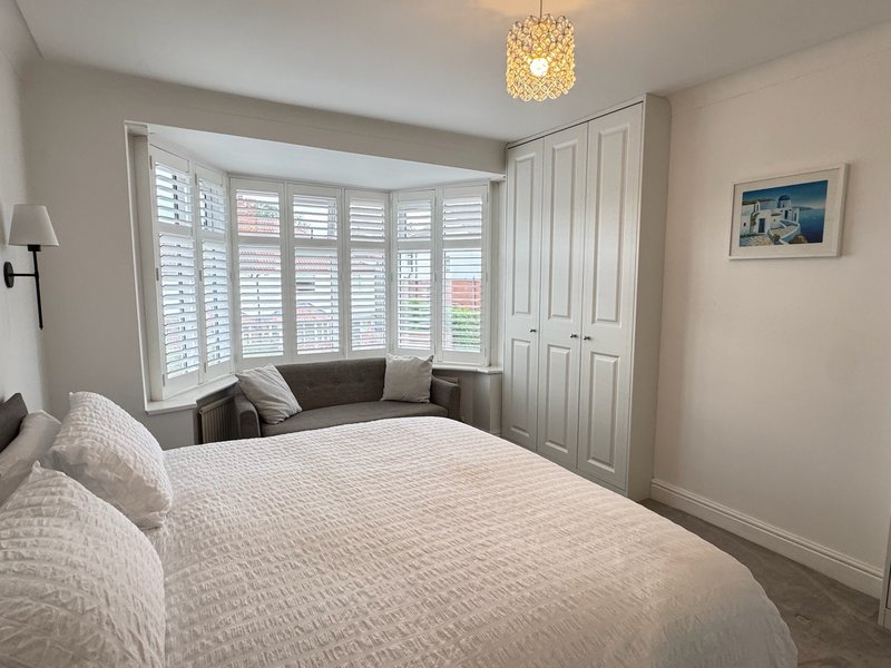 Bright bedroom with double bed, bay window with shutters, and pendant ceiling light