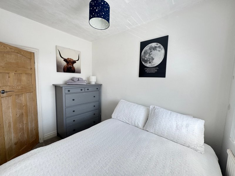 Bright bedroom with white bedding, gray dresser, wooden door and wall art