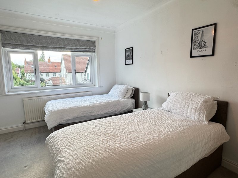 Twin bedroom with two single beds, window overlooking residential area, framed wall art