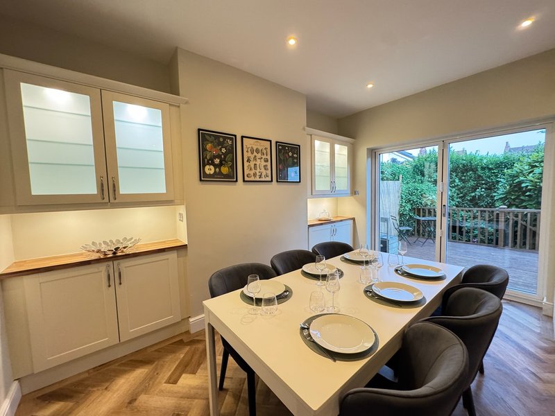 Dining room with white table, black chairs, kitchen cabinetry and glass doors to deck