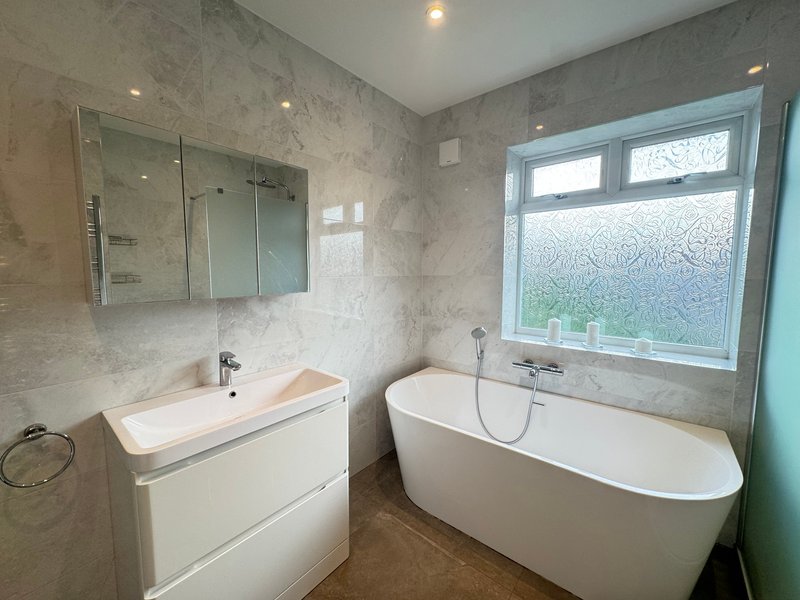 Modern bathroom with freestanding bathtub, floating vanity sink, and frosted window