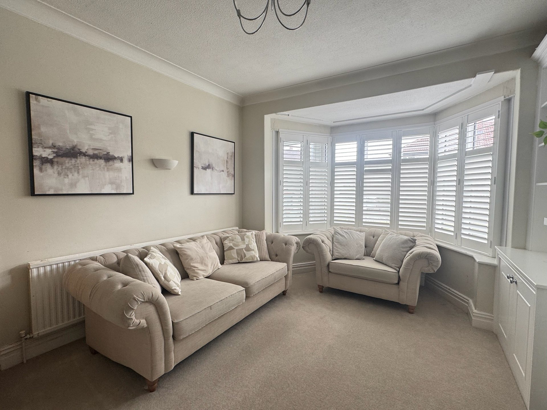 Bright living room with cream sectional sofa, framed wall art, shuttered windows and neutral carpet