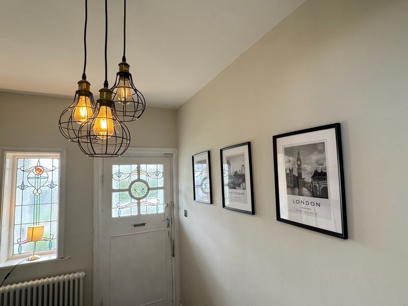 Bright hallway with pendant lights, white door, radiator and framed city photographs on wall