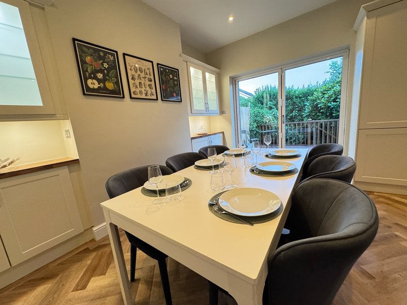 Modern dining room with white table, black chairs, framed wall art, and garden views