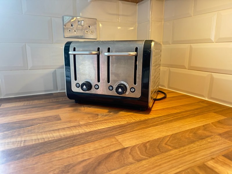 Kitchen countertop with four-slot toaster, wooden floor and cream tiled backsplash