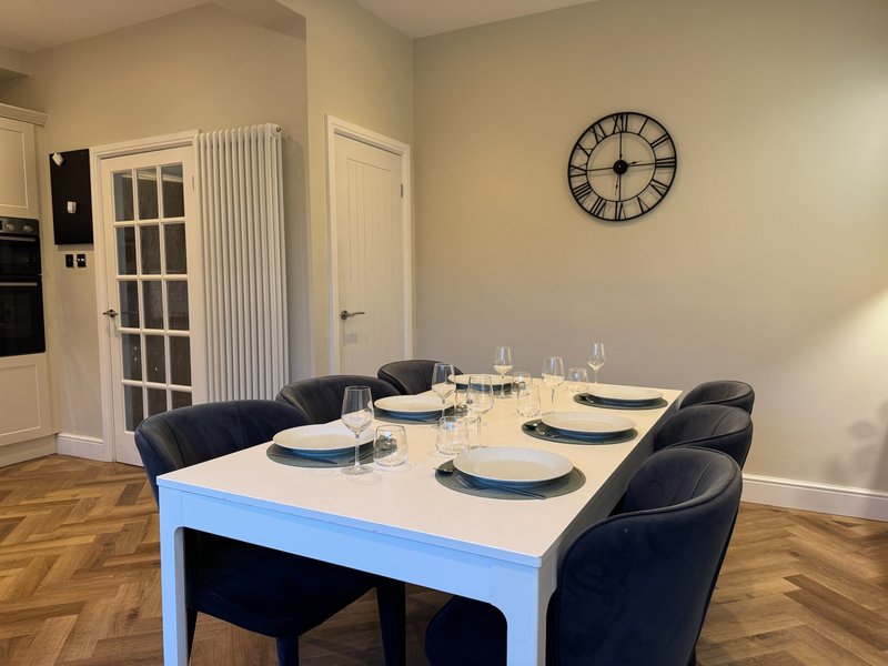 Dining room with white table, black chairs, place settings, and wall clock