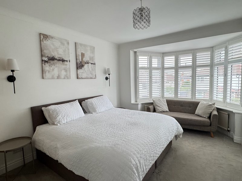Bright bedroom with double bed, grey sofa, shuttered windows and pendant light