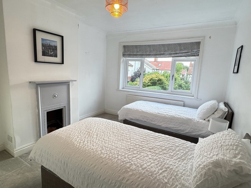 Bright bedroom with two single beds, fireplace, window with garden view, framed artwork
