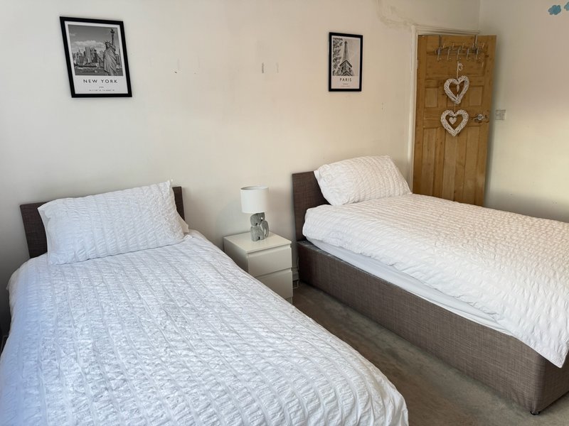 Twin bedroom with two single beds, white bedding, wooden door with heart decorations, framed wall art