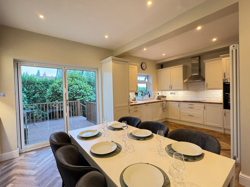 Modern kitchen-diner with cream cabinetry, dining table set for four, and glass doors to deck