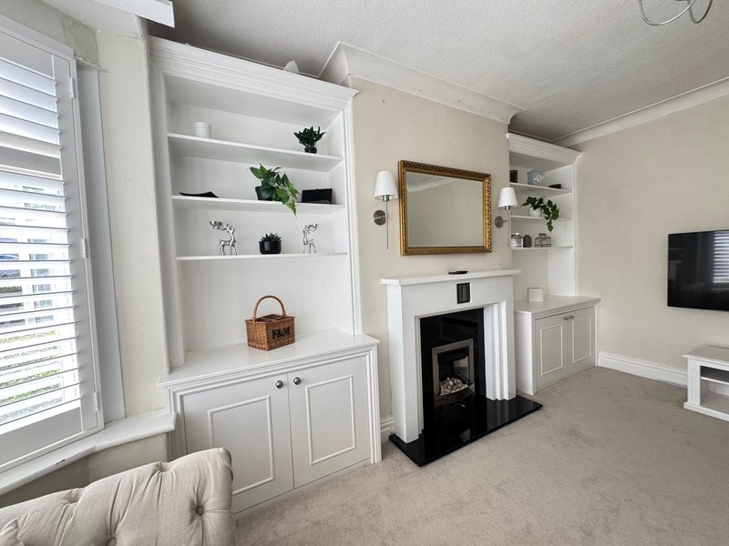 Bright living room with fireplace, white shelving, framed mirror and neutral decor