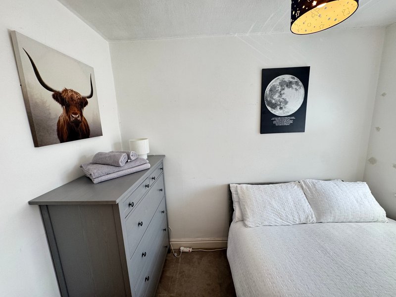Compact bedroom with single bed, gray dresser, wall art, and pendant light fixture
