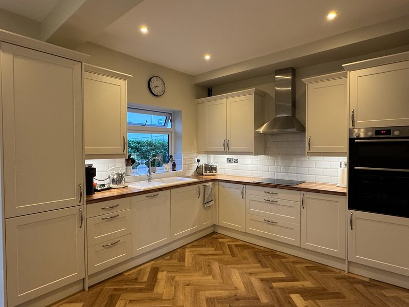 Modern kitchen with cream cabinetry, white subway tile backsplash, wooden herringbone flooring and window view.
