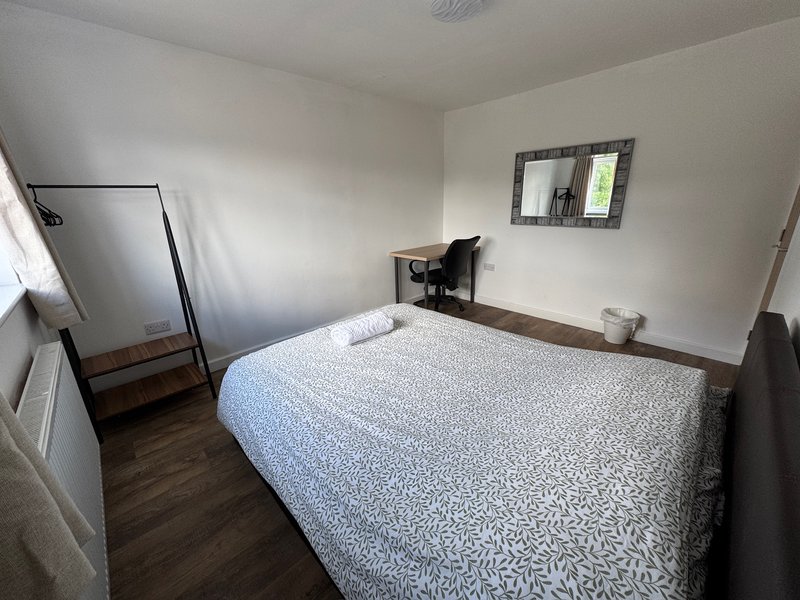 Bright bedroom with double bed, desk chair, mirror, and wooden flooring throughout