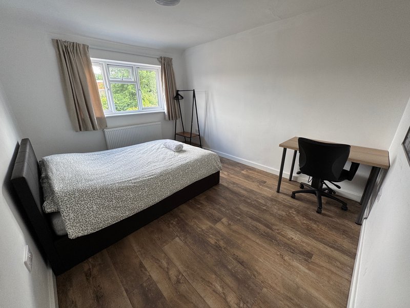 Bedroom with single bed, desk, chair, wooden floor and large window with curtains