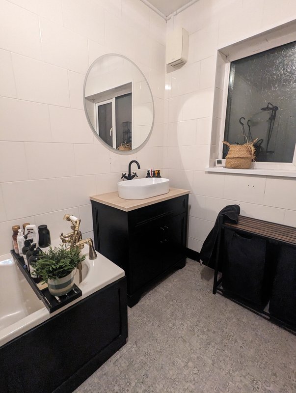 Modern bathroom with black vanity, round mirror, white tiles, potted plants and bathtub