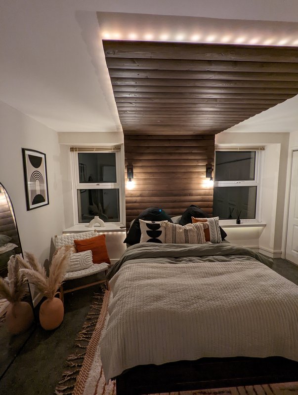 Modern bedroom with double bed, wood-slat accent wall, ambient ceiling lighting and two windows