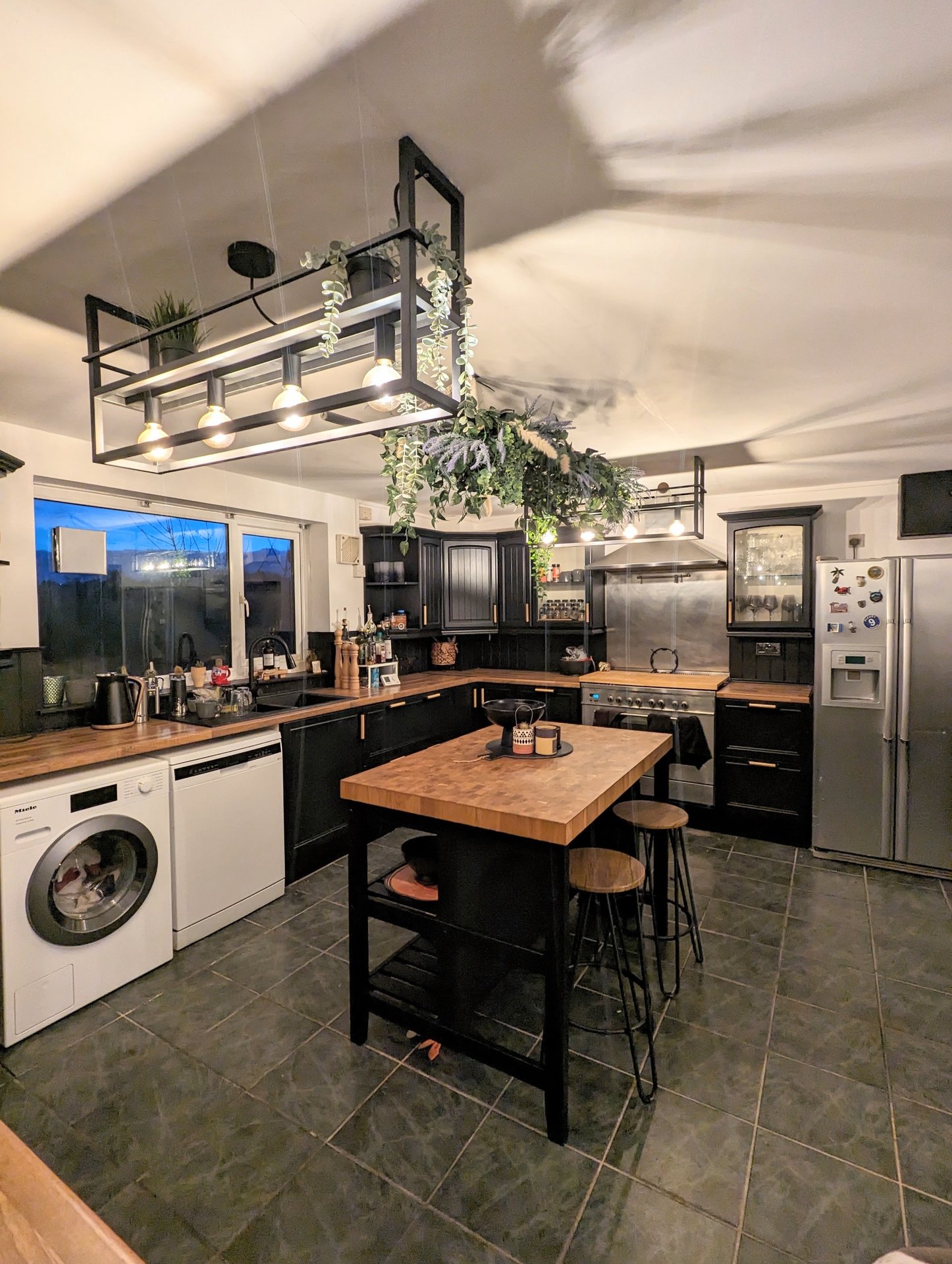 Modern kitchen with black cabinetry, wooden island, stainless steel appliances and pendant lighting
