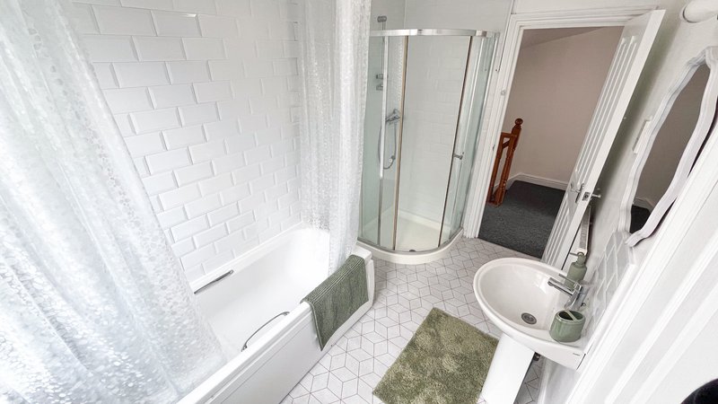 Clean bathroom with white subway tile walls, bathtub, sink, mirror and green bath mat