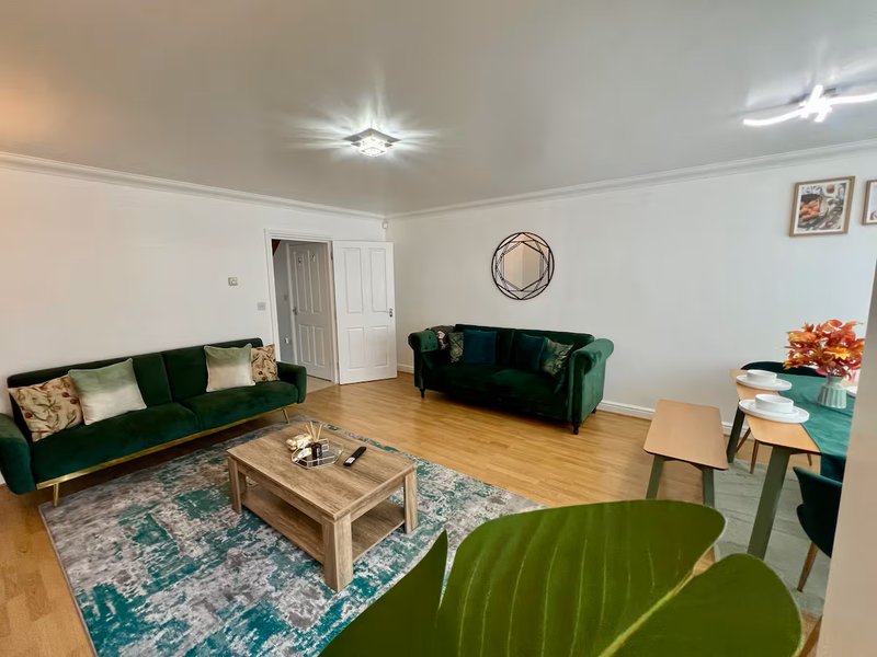 Spacious living room with green velvet sofas, wooden coffee table, and hardwood flooring