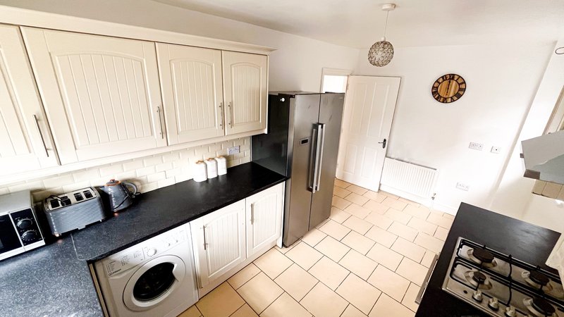 Modern kitchen with white cabinetry, black countertops, stainless steel appliances and tiled flooring