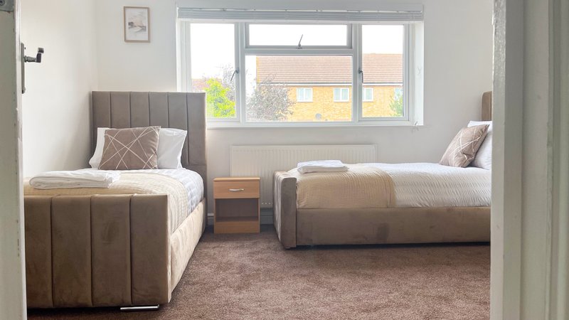 Twin bedroom with two single beds, wooden nightstand, window with street view