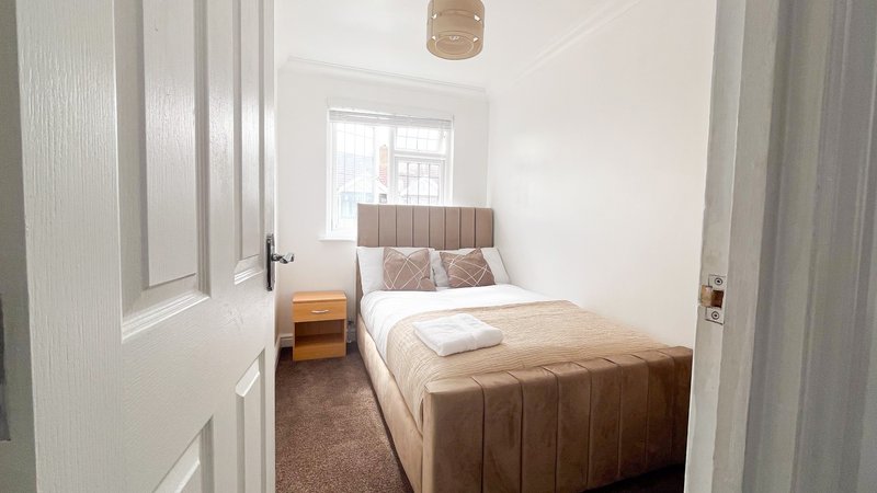 Small bedroom with brown upholstered bed, wooden nightstand, white walls and window