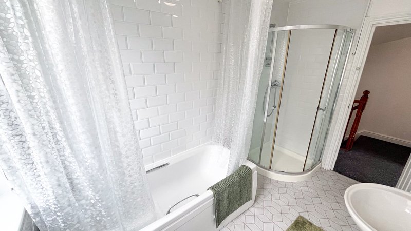 Bathroom with white subway tile walls, bathtub with shower curtain, curved glass shower enclosure, and toilet