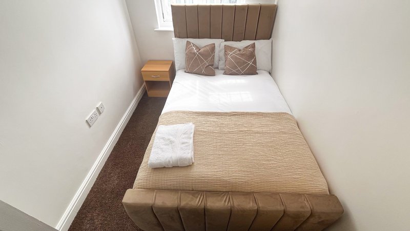 Compact bedroom with single bed, brown headboard, white pillows and bedside table