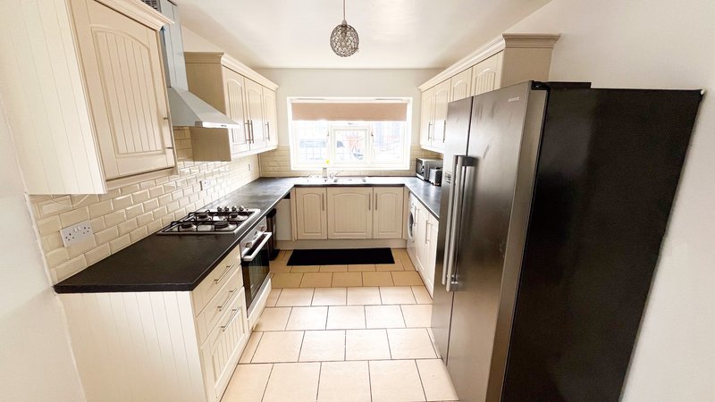 Modern kitchen with cream cabinets, black countertops, stainless steel appliances and tiled flooring