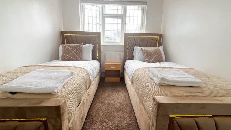 Twin bedroom with two single beds, wooden frames, neutral bedding and window with shutters