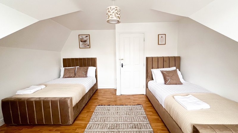 Twin bedroom with two brown upholstered beds, wooden floor, white door and vaulted ceiling