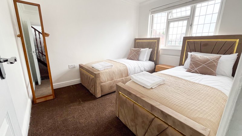 Bright bedroom with two single beds, wooden frames, brown carpet and tall mirror