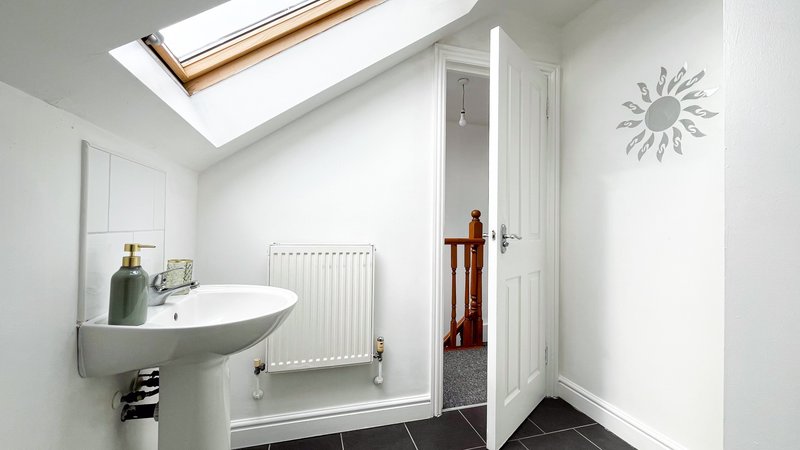 Modern bathroom with pedestal sink, radiator, skylight and dark tile flooring