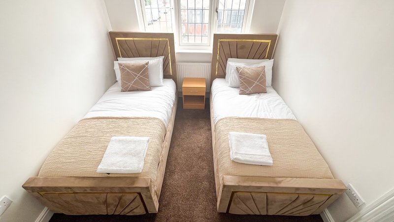 Twin bedroom with two single beds, wooden frames, white pillows and neutral bedding