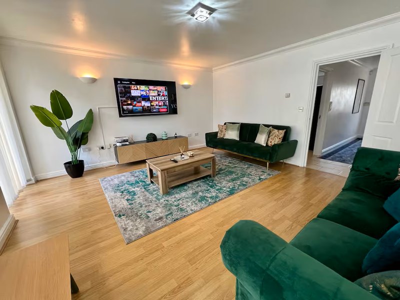 Spacious living room with green velvet sofas, wooden coffee table, TV, and potted plant