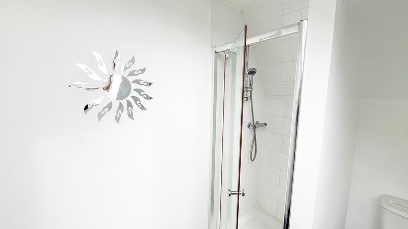 Modern bathroom with glass shower enclosure, white tile walls and decorative clock