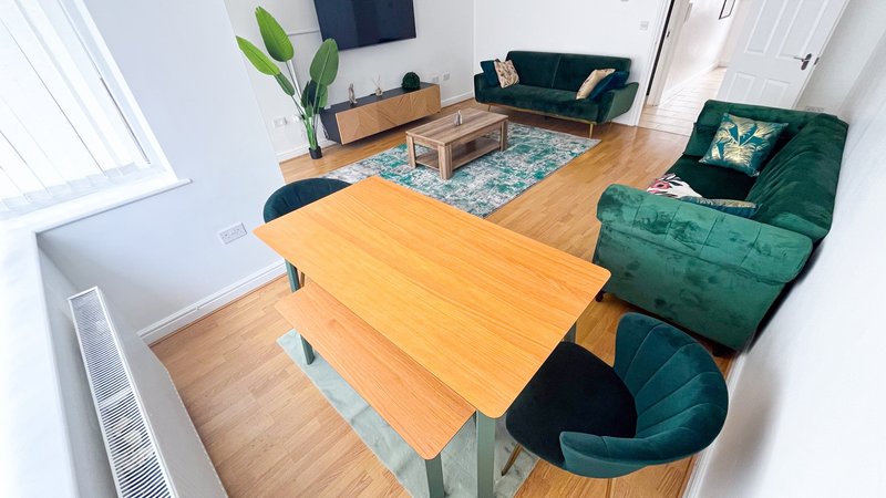 Open-plan living room with yellow dining table, green velvet sofas, wooden floor and natural light