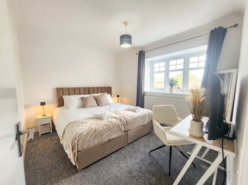 Modern bedroom with double bed, bedside tables, cream armchair and large window with blue curtains