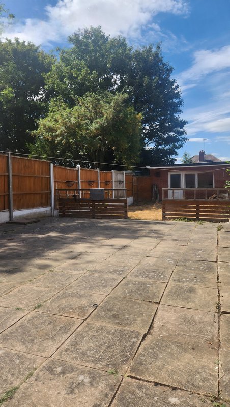 Outdoor courtyard with wooden fencing, paved ground, and mature trees overhead