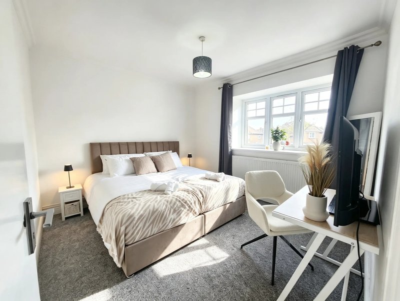 Bright bedroom with double bed, upholstered headboard, bedside lamps, armchair and large window