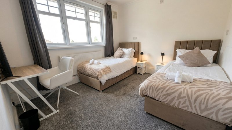 Twin bedroom with two beds, upholstered headboards, bedside tables, chair and window