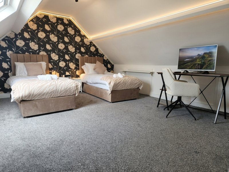 Attic bedroom with two single beds, patterned headboard, desk and landscape artwork on wall