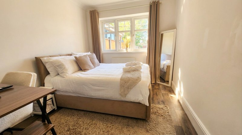 Bright bedroom with double bed, wooden desk, chair, mirror and large window with curtains