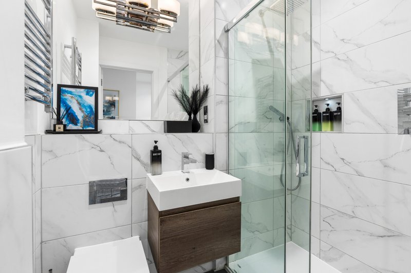 Modern bathroom with marble tiles, floating vanity, mirror, and glass shower enclosure