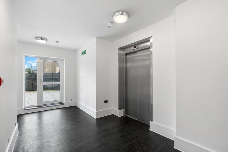 Modern building lobby with elevator, glass doors, dark flooring and white walls