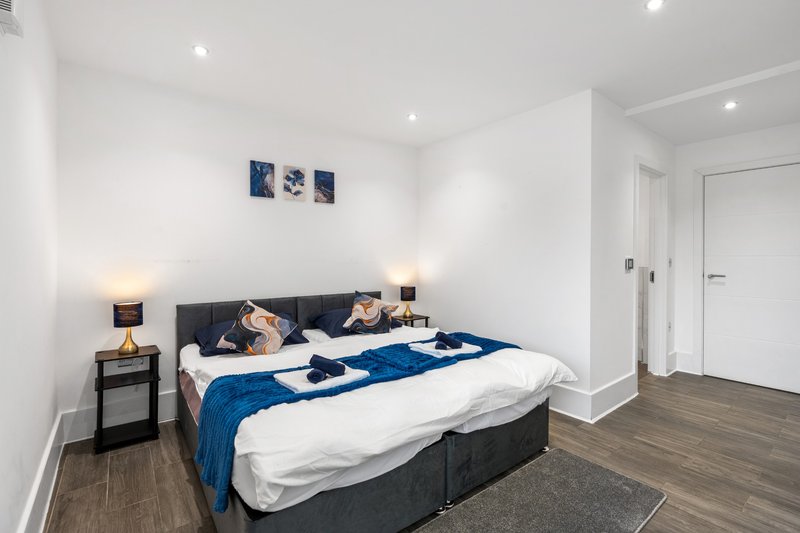 Modern bedroom with double bed, blue throw, dark headboard, bedside table and wall art
