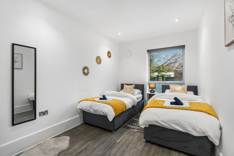 Twin bedroom with two single beds, yellow bedding, wooden flooring and wall-mounted mirror