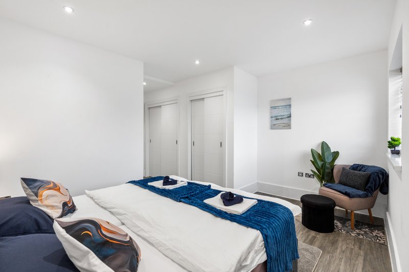 Modern bedroom with double bed, blue bedding, white wardrobe doors and potted plant
