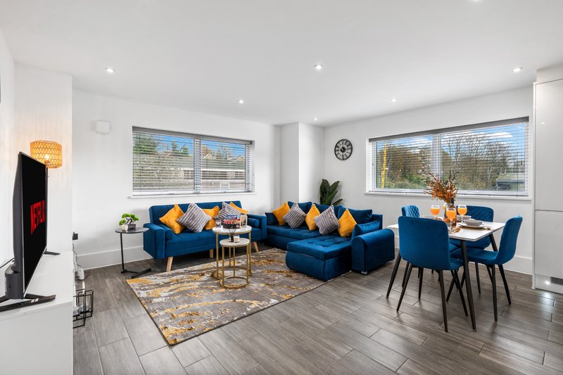 Modern open-plan living room with blue sectional sofa, dining table, and large windows